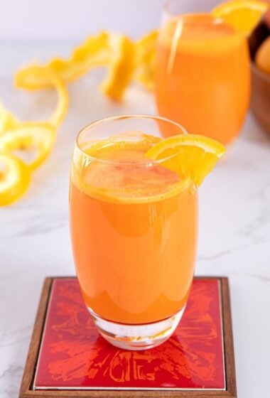 a glass of orange carrot juice with orange slices on top