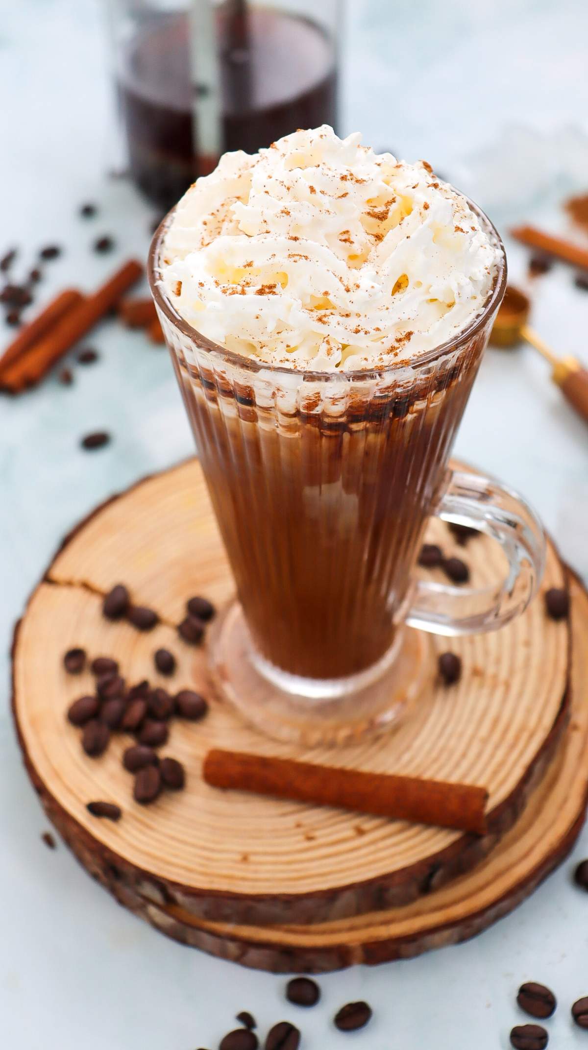 A slightly high-angle shot of an iced cinnamon dolce latte in a ribbed glass mug with a handle, served with a layer of whipped cream dusted with cinnamon, and syrup