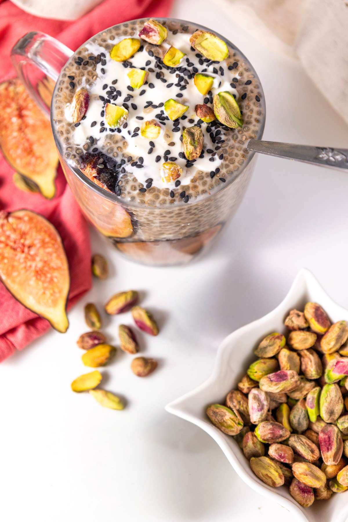 top-down view of a chia pudding glass topped with pistachios, black sesame seeds, and a dollop of yogurt with fresh figs