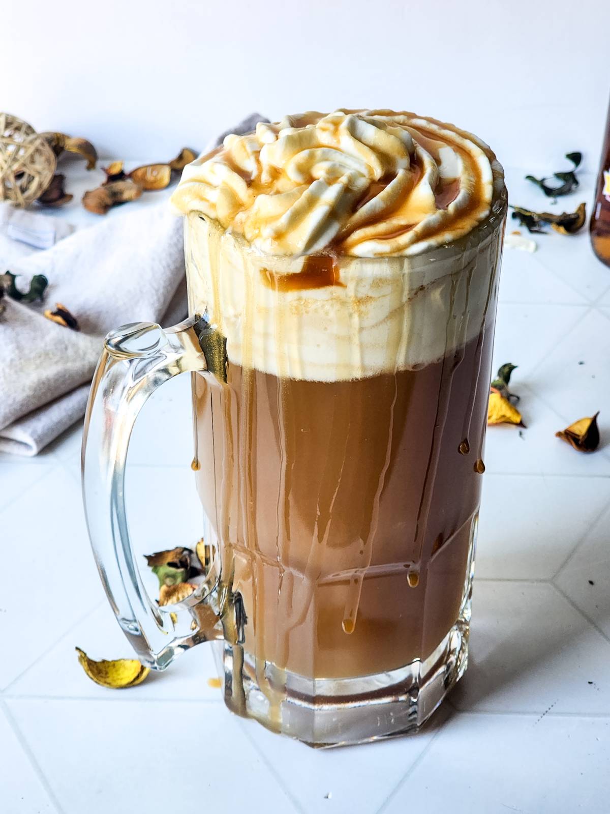 A close-up shot of Harry Potter Butterbeer in a clear glass mug, topped with whipped cream, caramel drizzle, and foam.