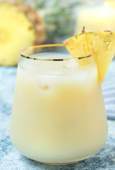 refreshing glass of Pera-Piña, a tropical drink made with pear and pineapple juice, garnished with a slice of pineapple, served over ice.