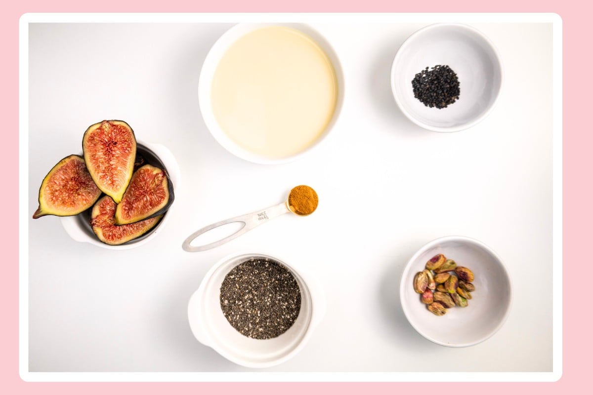 close-up shot of the ingredients for Fig Chia Pudding, arranged from a top-down angle. Fresh figs, chia seeds, turmeric powder, pistachios, and plant-based milk are placed in small bowls