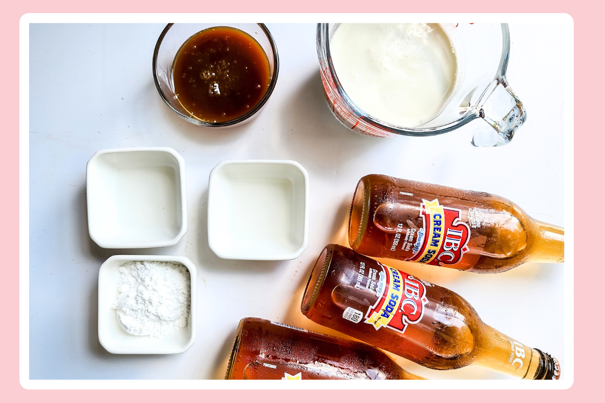 flatlay view of ingredients for making Harry Potter Butterbeer with two bottles of IBC cream soda, a small bowl of powdered sugar, a small container of milk, and a bowl with a rich brown syrup (likely caramel)